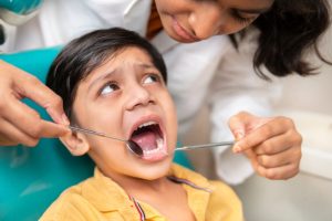 Little boy sitting on the dental chair with open mouth and a female dentist doing his oral checkup at dentist clinic.